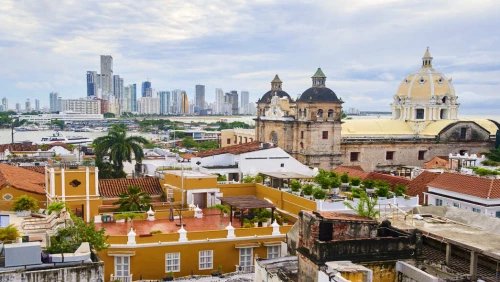 Vista aérea da cidade de Cartagena. No plano frontal, construções coloniais com cores vibrantes. Ao fundo, prédios altos e modernos.