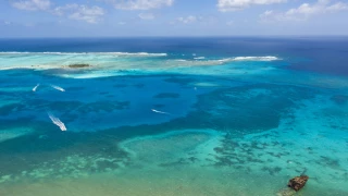 Vista aérea de um recife de coral com diferentes tonalidades de azul e verde, evidenciando as águas límpidas e as formações submarinas em San Andres