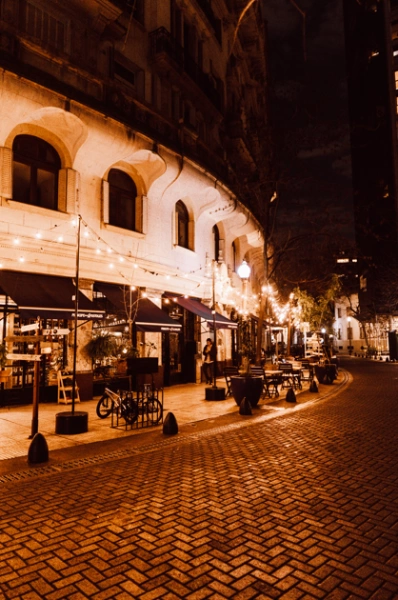 Fachada de um bar com varal de luzes acesas e mesas sobre a calçada, Retiro, Buenos Aires.