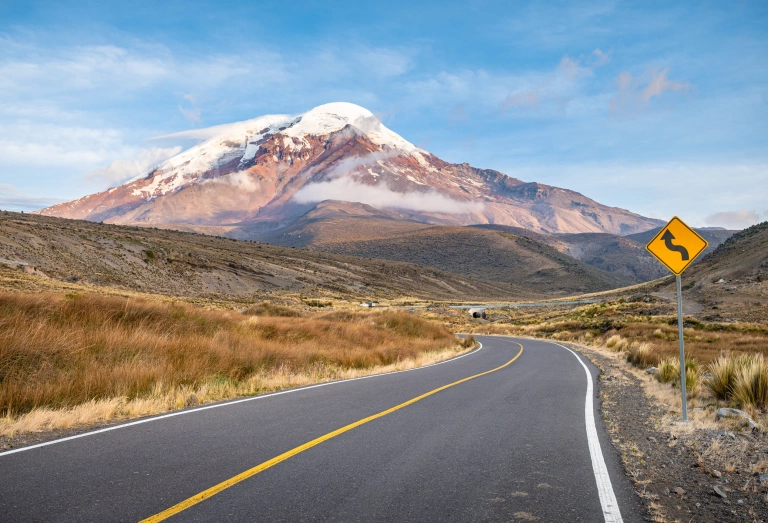 Estrada vazia com curva em direção e um vulcão com topo nevado